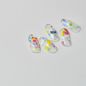 Macro shot of 5 transparent birthday nail tips with cake and bow relief designs