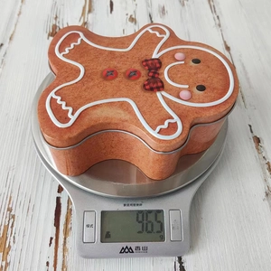 Macro shot of gingerbread man tin box weighing 96.5g on a scale for Christmas storage
