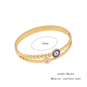 Detail of gold stainless steel bangle with blue and pink evil eye charms and wheat patterns
