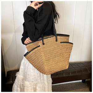 Detail of a straw tote bag showing black trim, side pockets and large capacity design