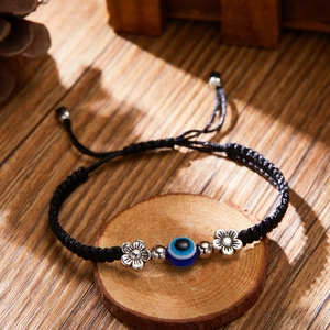 Close-up of black braided evil eye bracelet with blue bead on rustic wood slice