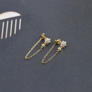 Detail of gold flower stud earrings with sparkling zircon tassels and elegant chain curve
