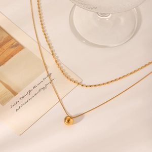 Detail of a double-layered gold stainless steel necklace with bead chain and ball pendant