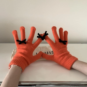 Close-up of orange knitted touchscreen gloves with cute black bow detail decorations