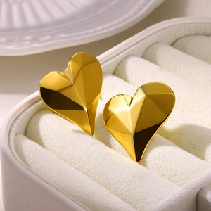 Macro view of gold heart stud earrings with geometric facets in a white jewelry box