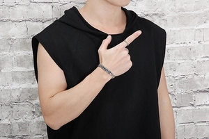 Close-up of a men's woven wheat chain bracelet and textured ring on a male model's wrist