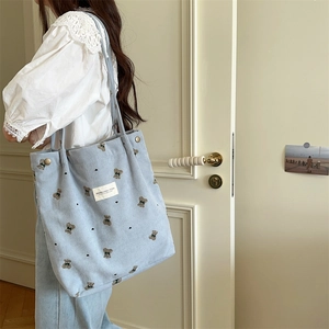 Light blue corduroy tote bag with bear embroidery shown in a casual lifestyle side view