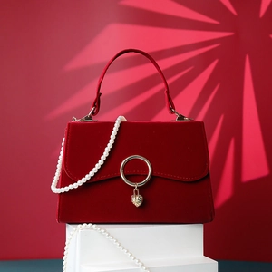 Detail of red velvet handbag with golden ring heart pendant and pearl strap