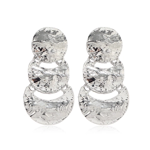 Détail macro de boucles d'oreilles géométriques argentées en métal martelé à trois couches
