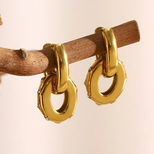 Detailed view of two-tone gold earrings with oval zircon charms on a natural branch