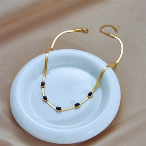 Gold snake chain necklace with five black oval gemstones on a white ceramic plate
