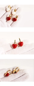 Close-up of heart-shaped hoop earrings featuring red and white enamel on gold metal