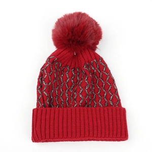 Close-up of red knit beanie with silver wave patterns and a fluffy faux fur pom-pom detail