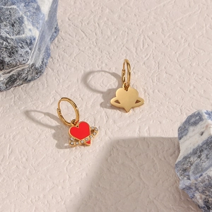 Detail of gold asymmetric earrings featuring a red enamel heart and crystal Saturn charm