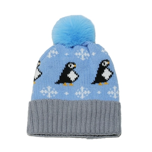 Light blue winter knit hat with penguin pattern, white snowflakes, and a faux fur pompom