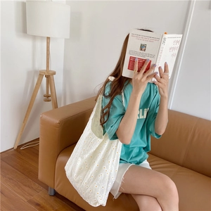Lifestyle view of a white canvas tote bag with yellow daisy prints on a leather sofa