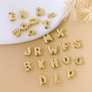 Macro shot of gold-plated 18K copper alphabet beads on a textured surface