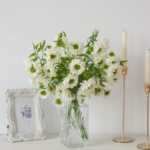 Detailed white artificial daisies in a glass vase with elegant vintage frame and gold candles