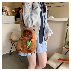 Close-up of a brown plush capybara bag featuring an orange flower accessory on the model