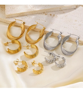 Collection of gold and silver C-shaped hoop earrings on textured stone and beige fabric