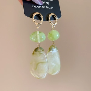 Detail of drop earrings with light green resin pendant and golden irregular ring stud