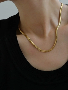 Close-up of a gold herringbone snake chain necklace on a model wearing black