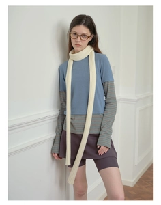 Detail of a beige knit long scarf paired with a layered blue tee and striped undershirt