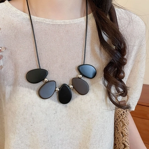 Detail of wooden resin pendant necklace with silver beads on a beige knit sweater