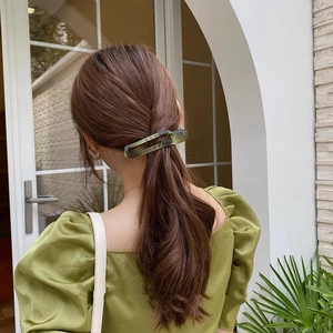 Deep green matte shark hair clip holding a classic updo on a model, outdoor street view