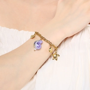 Détail du bracelet doré avec pendentifs coquillage, tortue et poisson au style marin