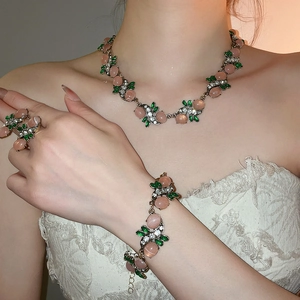 Elegant jewelry set detail with pink gems and green leaf accents worn by a model