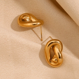 Macro shot of 18K gold plated stainless steel knot stud earrings on beige silk fabric