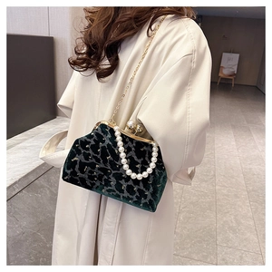Detail of dark green velvet shell bag featuring pearl handle and gold chain strap