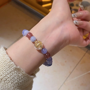 Detail of beaded stretch bracelet featuring lavender and brown beads with a golden coin charm