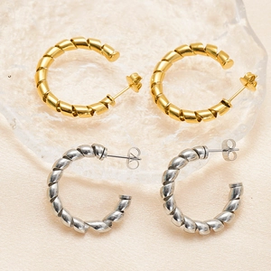Detail of twisted hoop earrings in gold and silver finish on textured glass surface