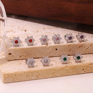 Elegant silver flower stud earrings with colorful crystals on a beige stone display