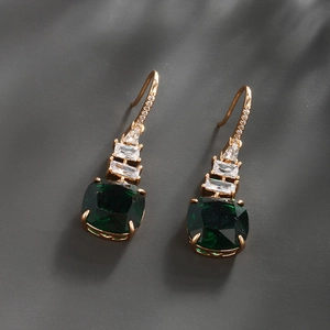 Macro shot of gold emerald drop earrings with sparkling white zircons on dark background