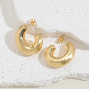 Close-up of chunky golden C-shaped brass hoop earrings with metallic texture on stone