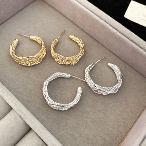 Macro shot of gold and silver woven texture hoop earrings in a gray jewelry box