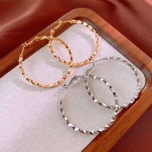 Detailed view of large gold and silver hoop earrings with diamond-cut faceted textures