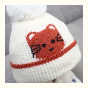 Detail of white knitted kids beanie with orange cat pattern and a fluffy pompom