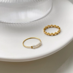 Detail of French minimalist gold pearl ring and geometric checkered ring on ceramic tray
