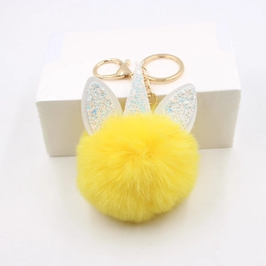 Sparkly unicorn pom pom keychain with a soft yellow fluffy ball and gold metal hardware
