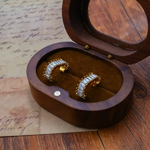 Close-up of golden C-shaped hoop earrings with baguette-cut zircon in a wooden box