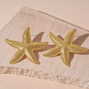 Detailed macro view of golden starfish earrings with textured finish on a stone surface