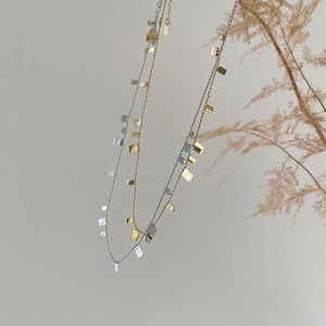 Detailed close-up of gold and silver square sequin necklaces with dried floral accents