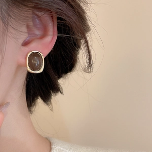 Close-up of retro square earrings with gold metal frame and brown resin on model's ear