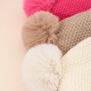 Gestrickte Kindermützen für den Winter mit flauschigen Bommeln in Rosa und Beige