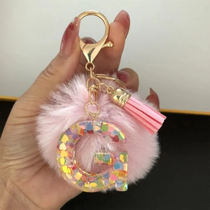 Detail of resin letter G keychain with pink pompom and colorful heart-shaped sequins