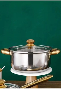 Close-up of stainless steel soup pot with golden handles on a white marble base